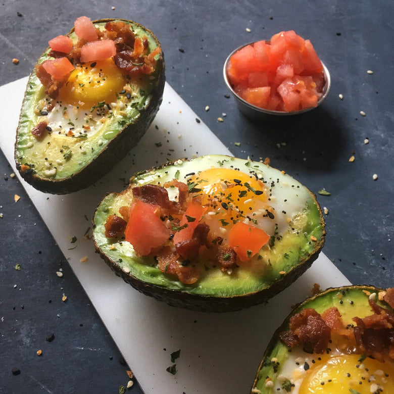 Avocado halves filled with sunny side up egg, tomatoes and bacon